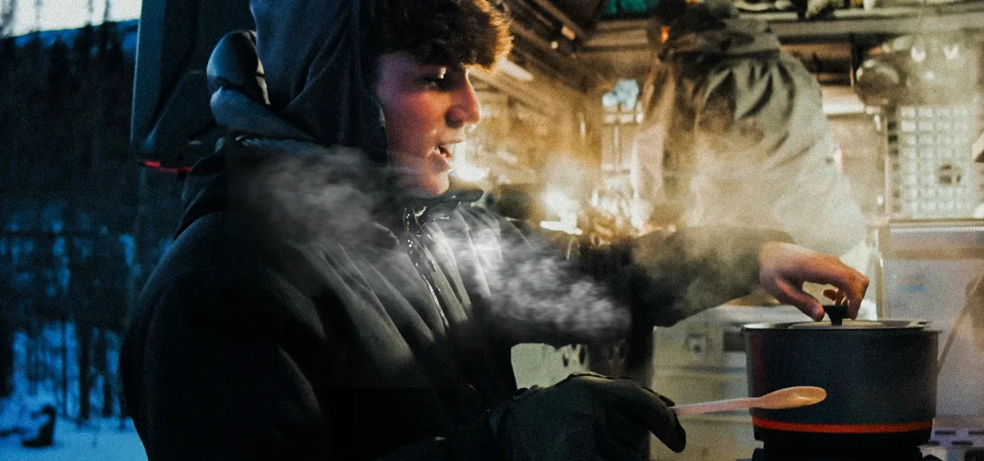 Person in winter gear using Stoke Voltaics kettle pot outdoors near snow, steam rising