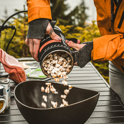 Portable electric kettle popcorn maker pouring popcorn into bowl outdoors on camping table